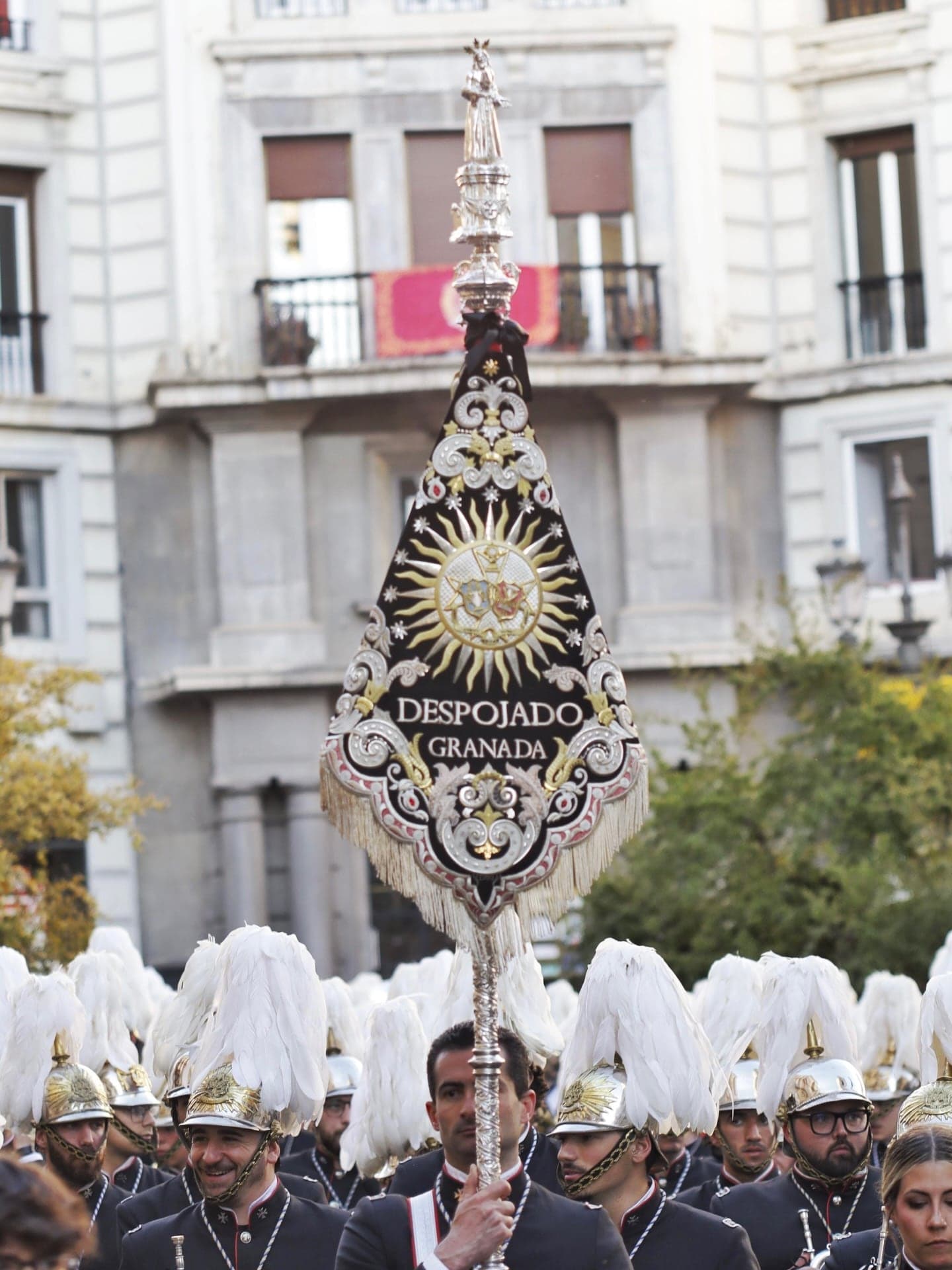 El banderín de la banda avanza por la calle San Antón sobre los cascos de penacho blanco