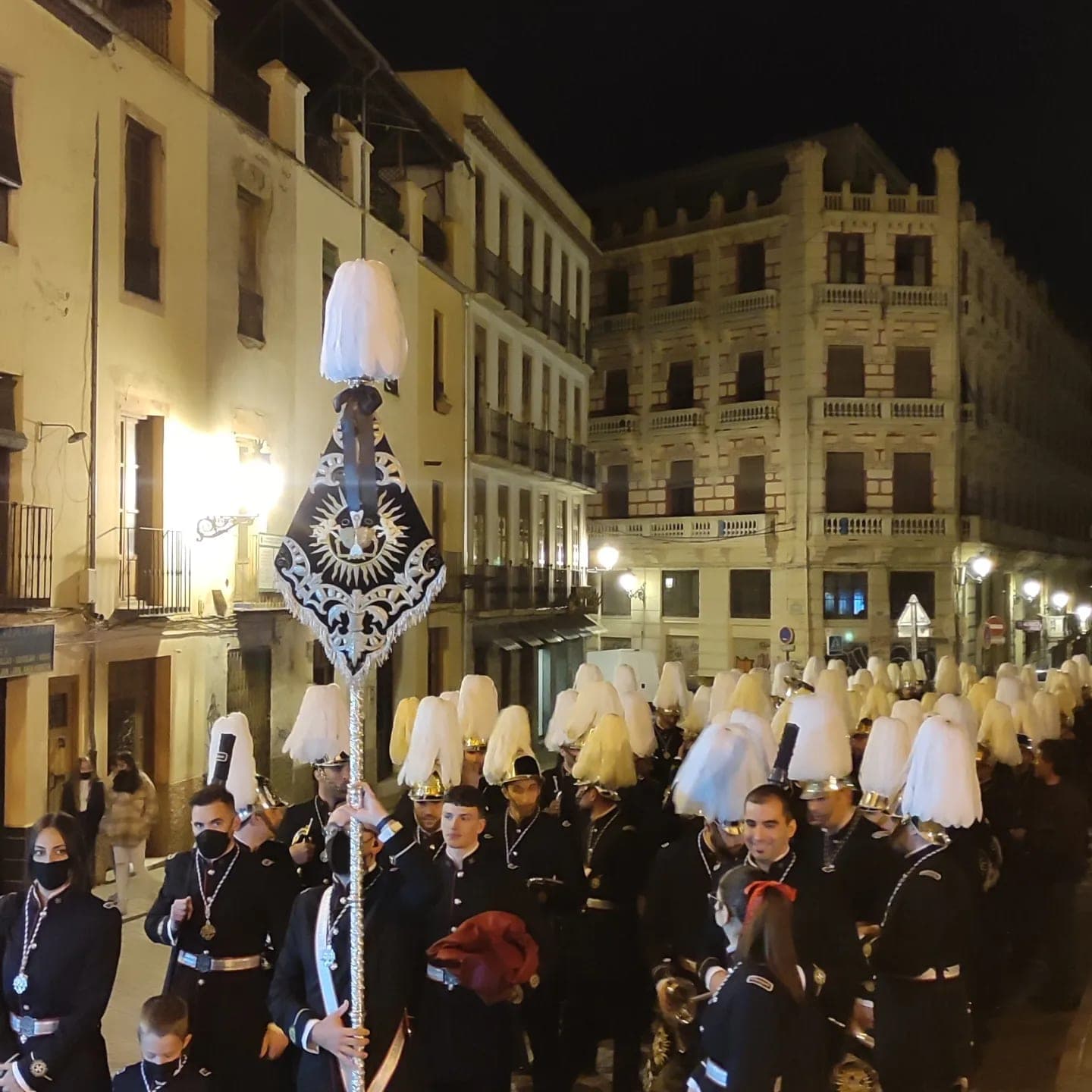 La banda, con los cascos de penacho blanco y el banderín, en la calle Pan de noche