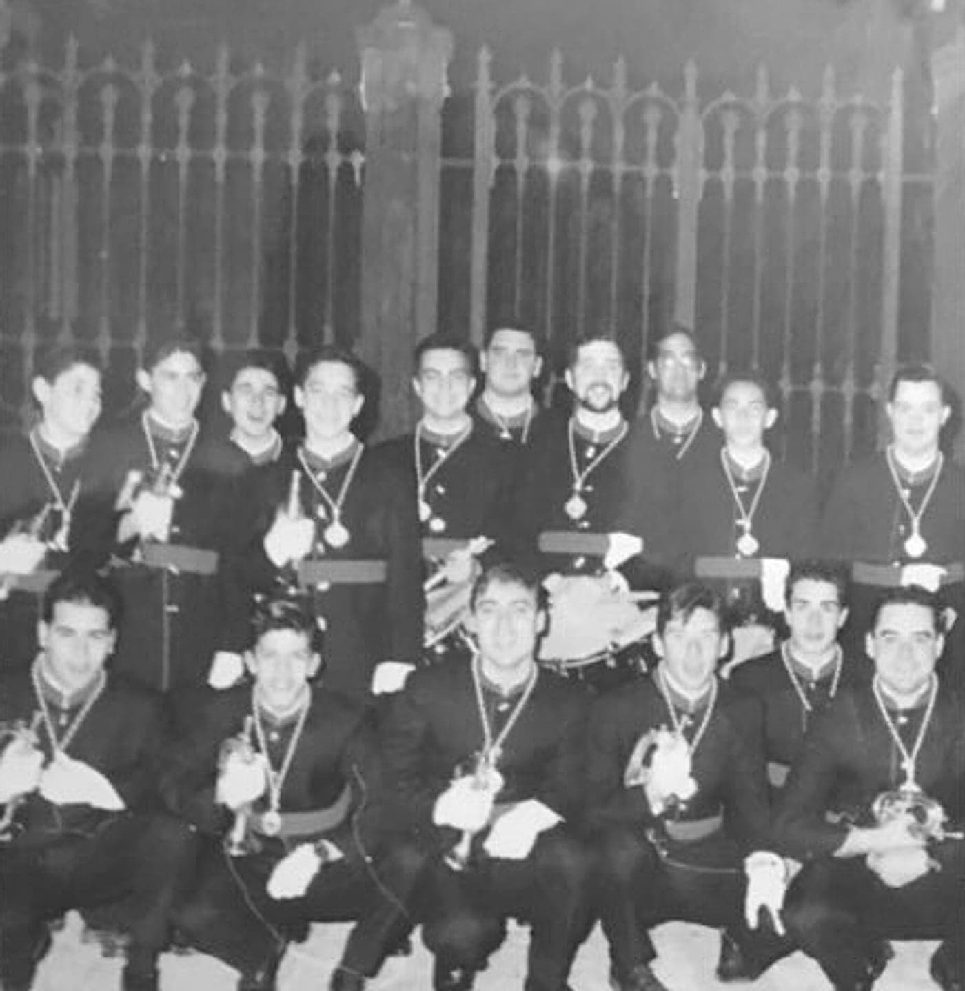 Foto en blanco y negro de los primeros componentes de la banda, uniformados ante una reja