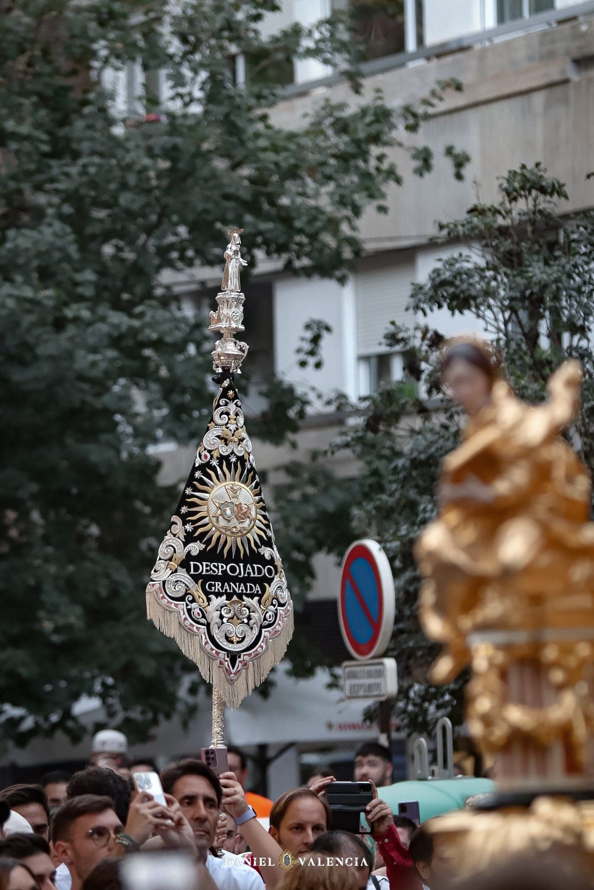 El banderín de la banda por las calles de Granada, rodeado de público